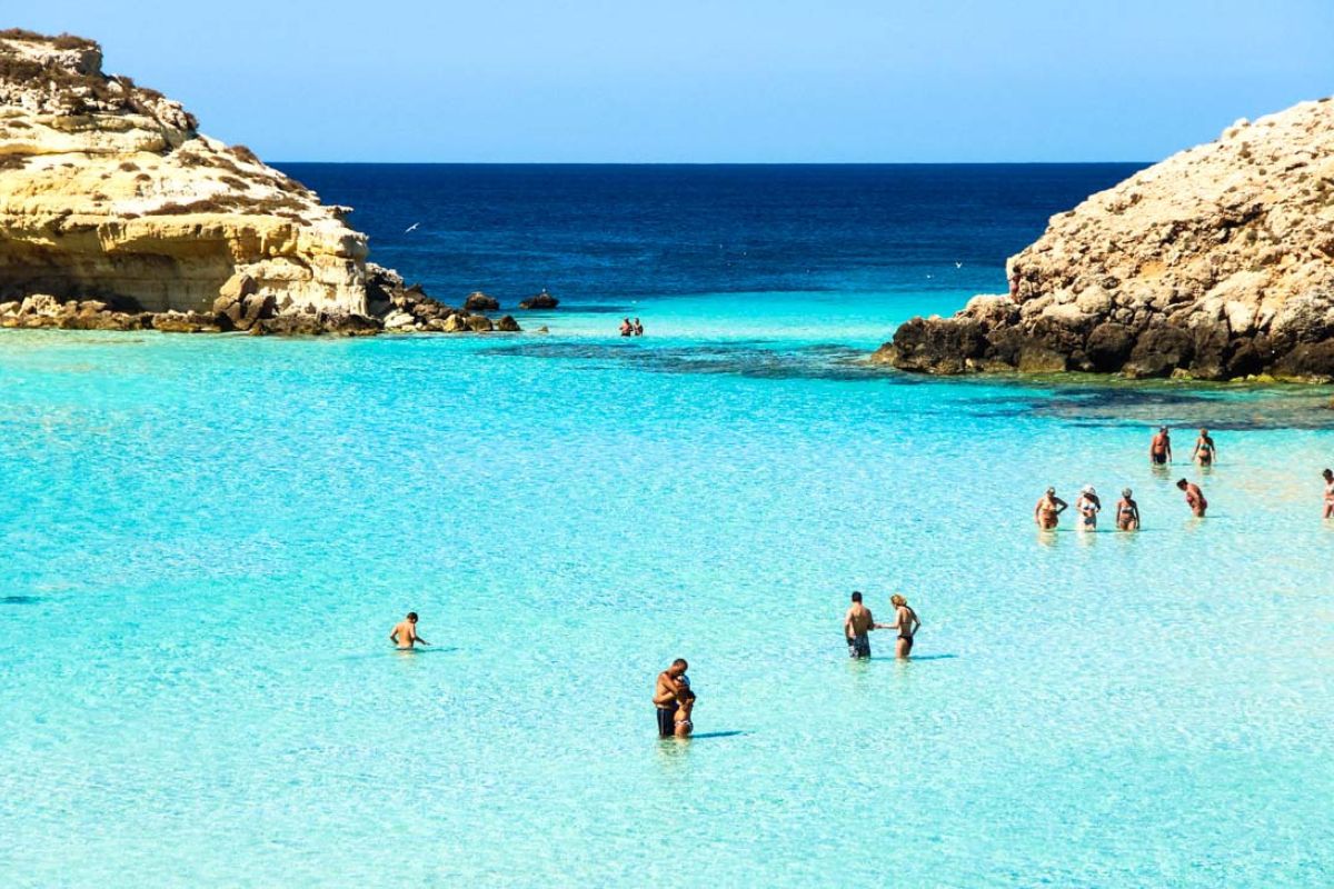 Festa tradizionale serale sulla spiaggia di Lampedusa, con lampade colorate e gente che balla, atmosfera estiva e mar Mediterraneo sullo sfondo