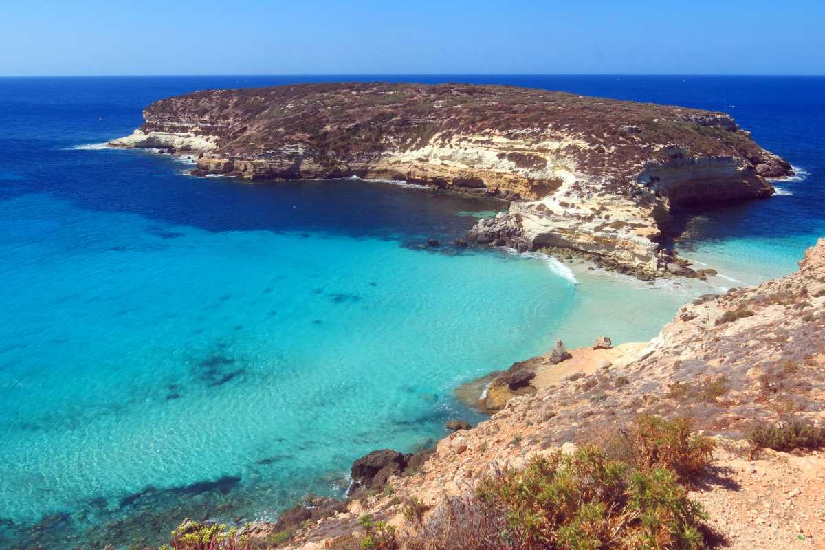 Bambini seduti a tavola in un ristorante all’aperto di Lampedusa, sorridenti, con piatti semplici e colorati, atmosfera familiare e rilassata